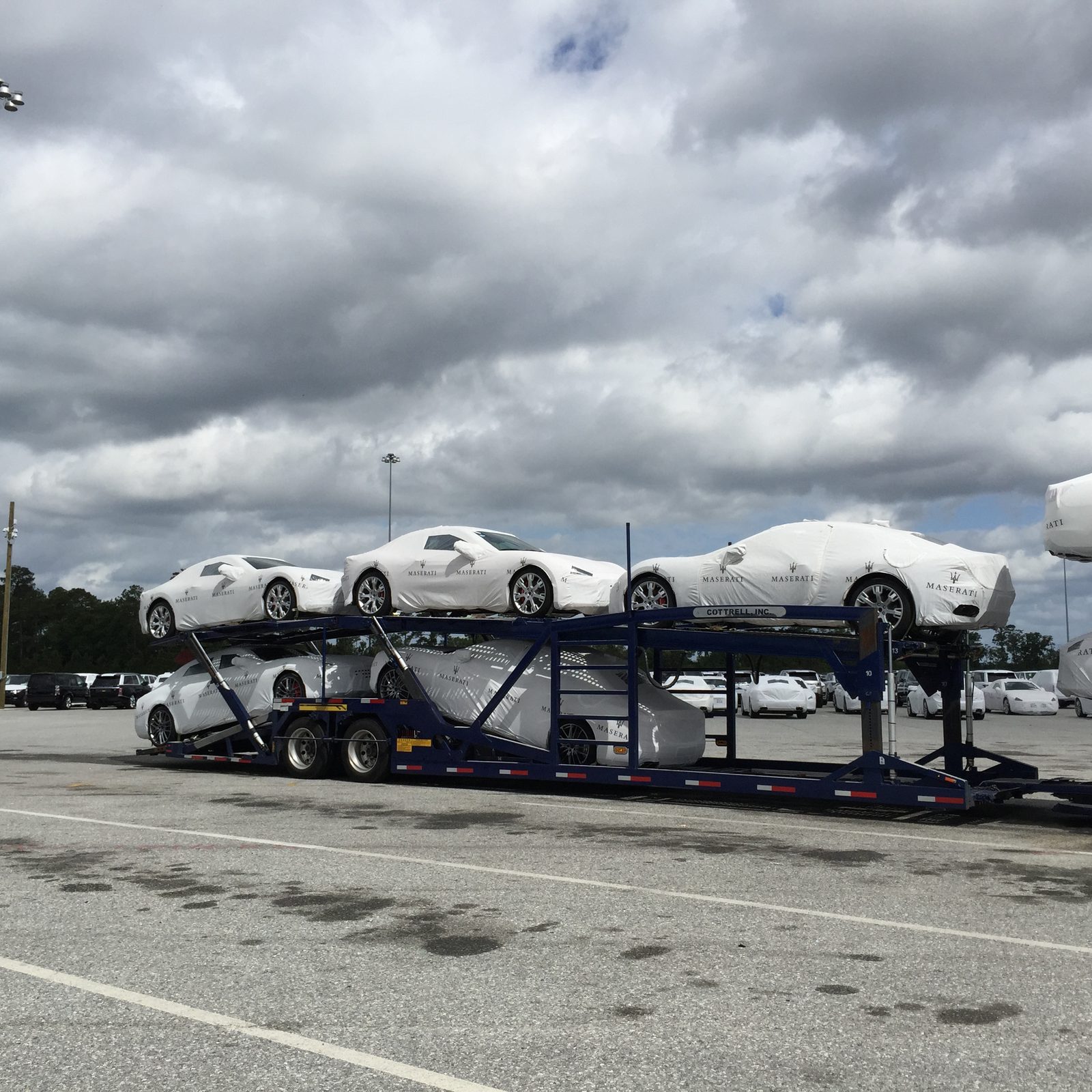 Car carrier loaded with white vehicles, strapped and covered for transit