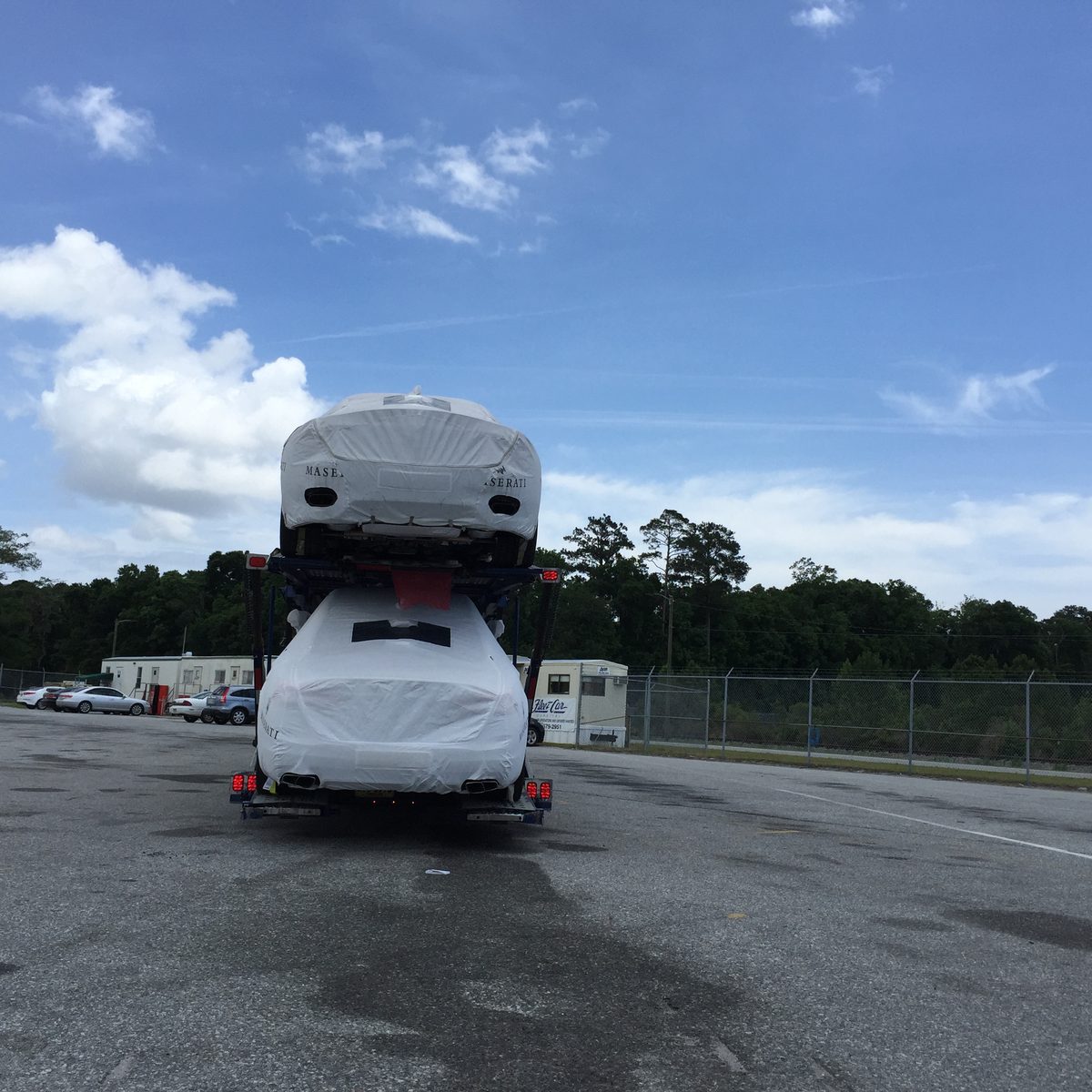Car transporter carrying two covered vehicles, photographed from behind